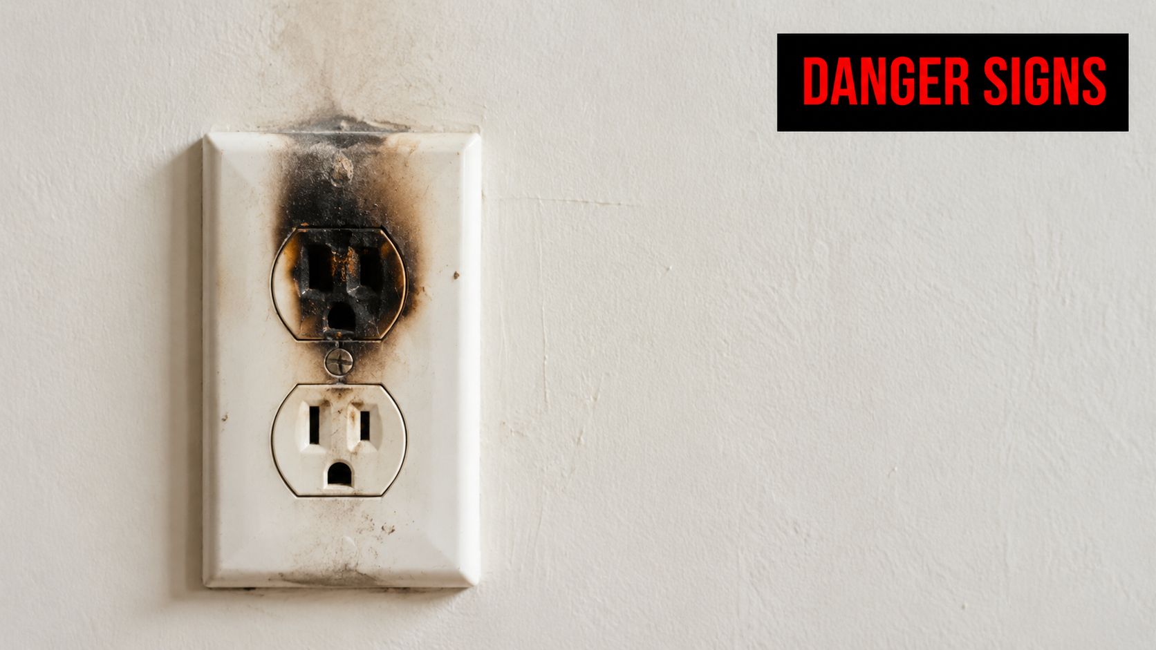 A close-up view of a damaged, scorched white electrical outlet on a wall indicating a fire hazard.